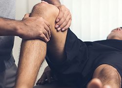 therapist treating injured knee of athlete male patient
